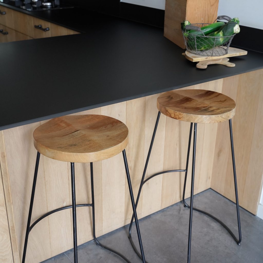 Zwart keukenblad met houten onderkasten en barstoelen