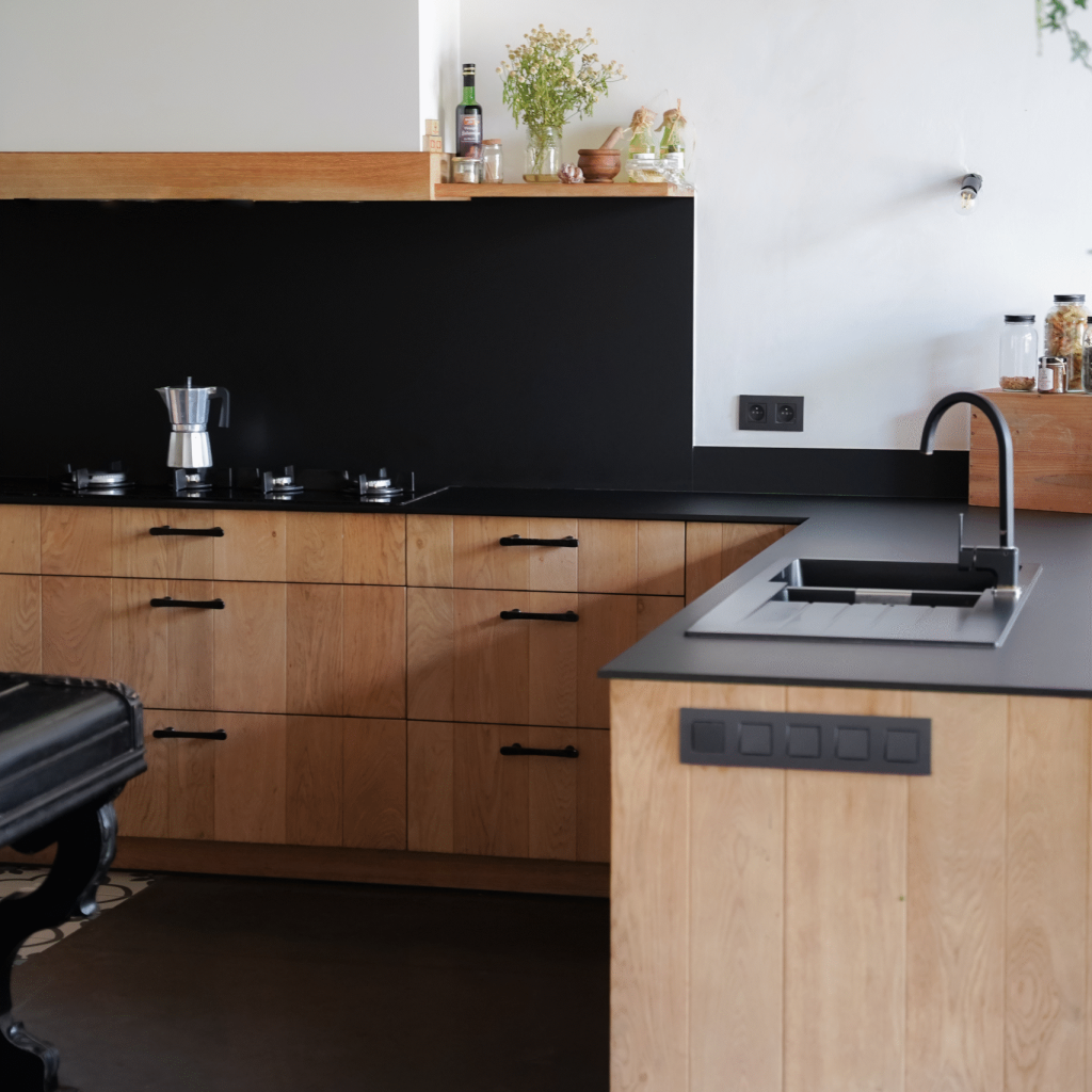 Keuken met zwart werkblad, houten lades en spatwand met legplank